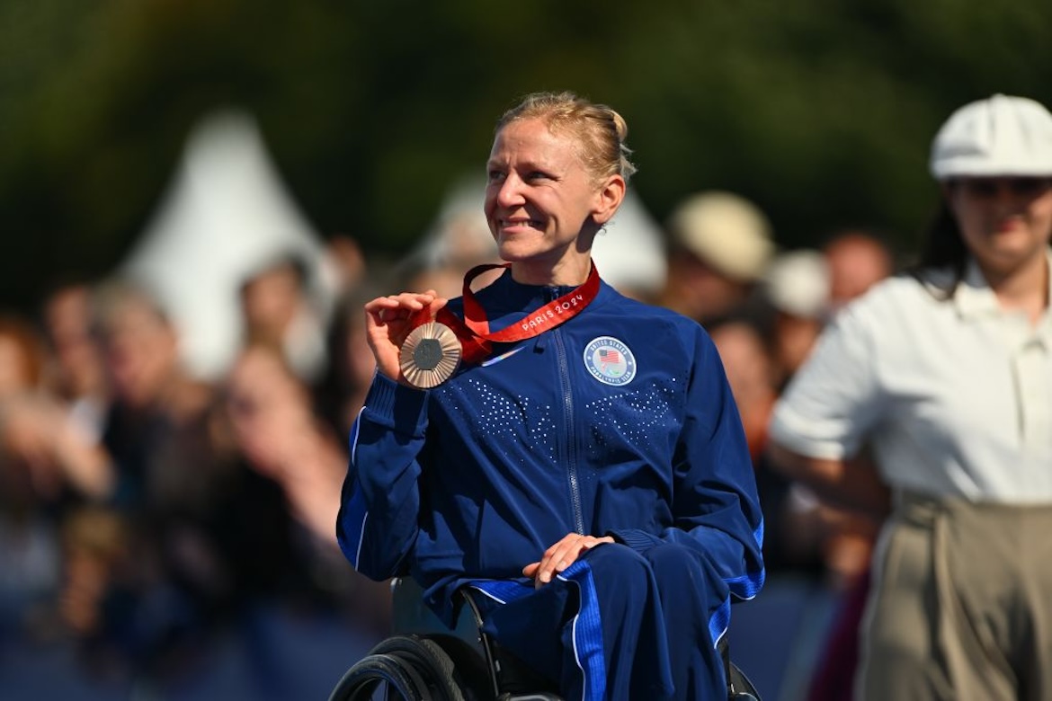 Foto da corredora profissional em cadeira de rodas Susannah Scaroni usando a medalha de bronze paraolímpica no pescoço